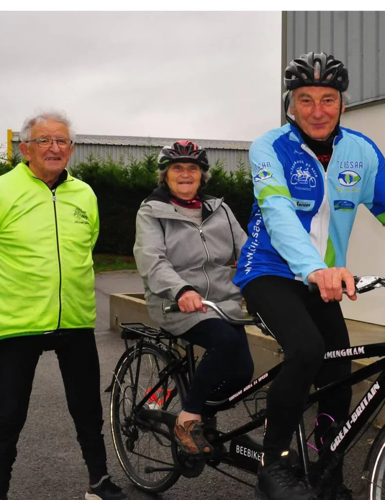 Sur la photo, Micheline est assise à l'arrière du tandem souriante et prête à avaler les kilomètres. A gauche, Léon en veste fluo. Le pilote du tandem, Jack Alain est habillé avec la superbe veste de vélo aux couleurs de la Clissaa. On sent ces deux tandemistes impatients de partir... juste après le sourire à la photographe de Ouest France.