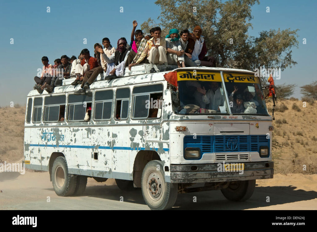 Un bus à la peinture écaillée en Inde, il est tellement plein de monde qu'il y en a aussi 15 sur le toit.
4 personnes debout à côté du chauffeur, on se demande comment il peut voir la route !